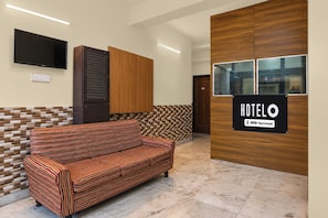 Zona de recepción de un hotel con un sofá, un televisor y un cartel que indica el nombre del hotel y el servicio OYO.