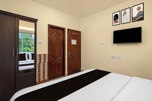 A hotel room with a bed, two wooden doors, a television, and artwork on the wall.