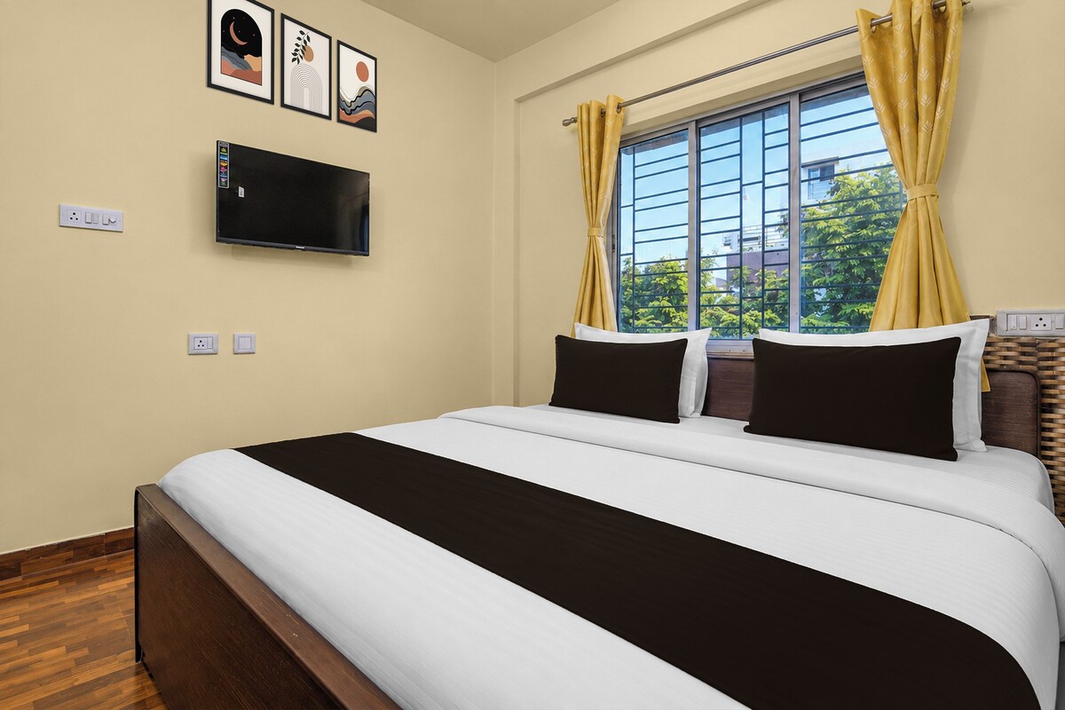Une chambre d’hôtel avec un lit, un téléviseur à écran plat fixé au mur et une fenêtre avec des rideaux.