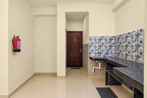 A hallway leading to a room with a door, a fire extinguisher mounted on the wall, and a tiled backsplash in the adjacent room. - Hotel O Biswa Bangla Gate  (Barasat)