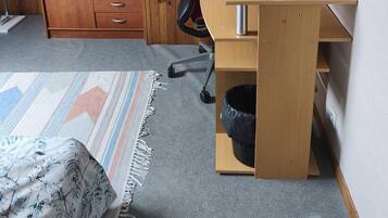 Une pièce comprenant un bureau en bois, une chaise, une lampe, une armoire et un tableau accroché au mur.