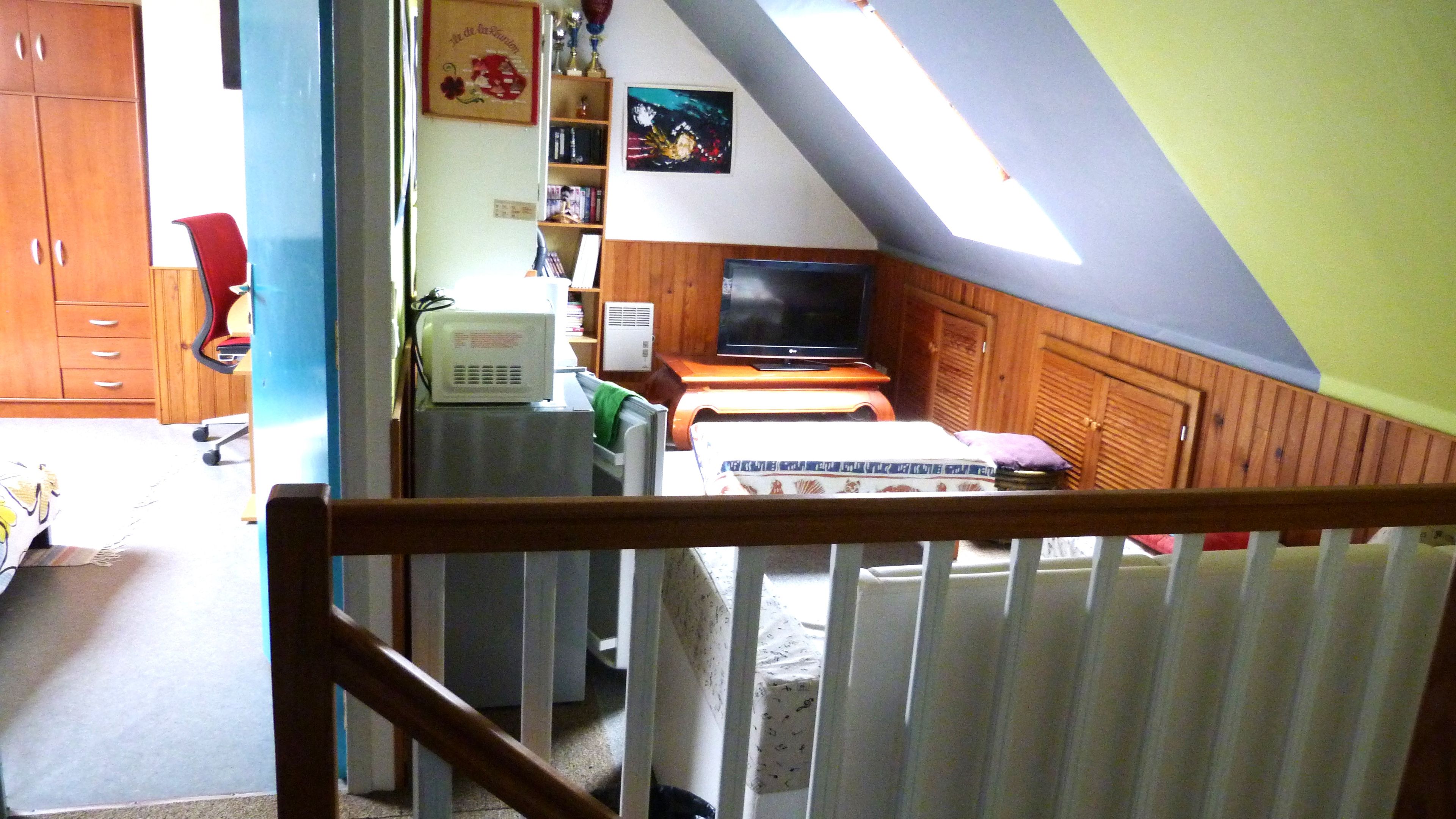 Ein Zimmer mit schrägen Wänden, einem Fernseher, einem Bett, einem Schreibtisch und einem Stuhl.