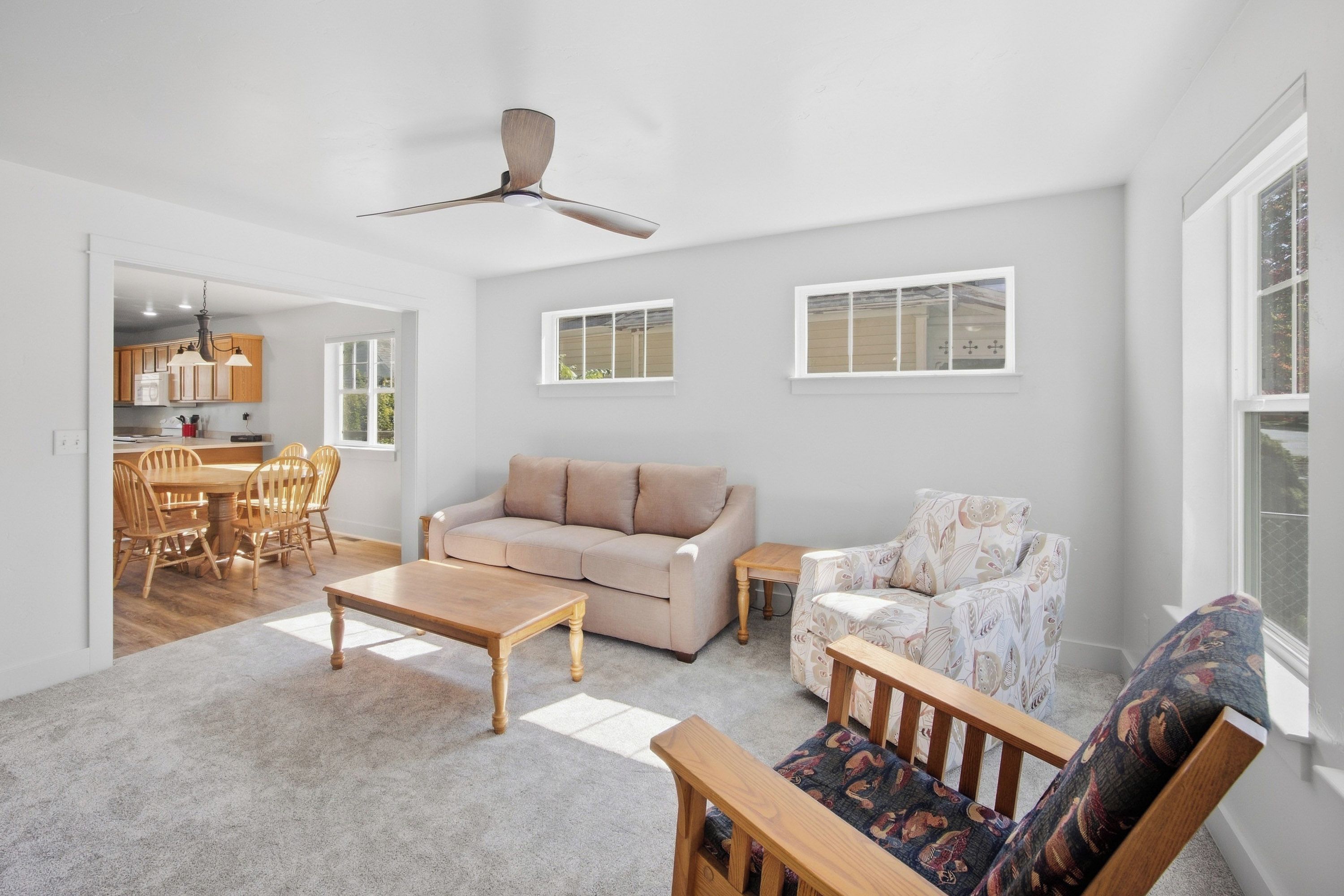 A spacious living room with a sofa, a patterned armchair, a wooden coffee table, and a dining area with wooden chairs and a table.