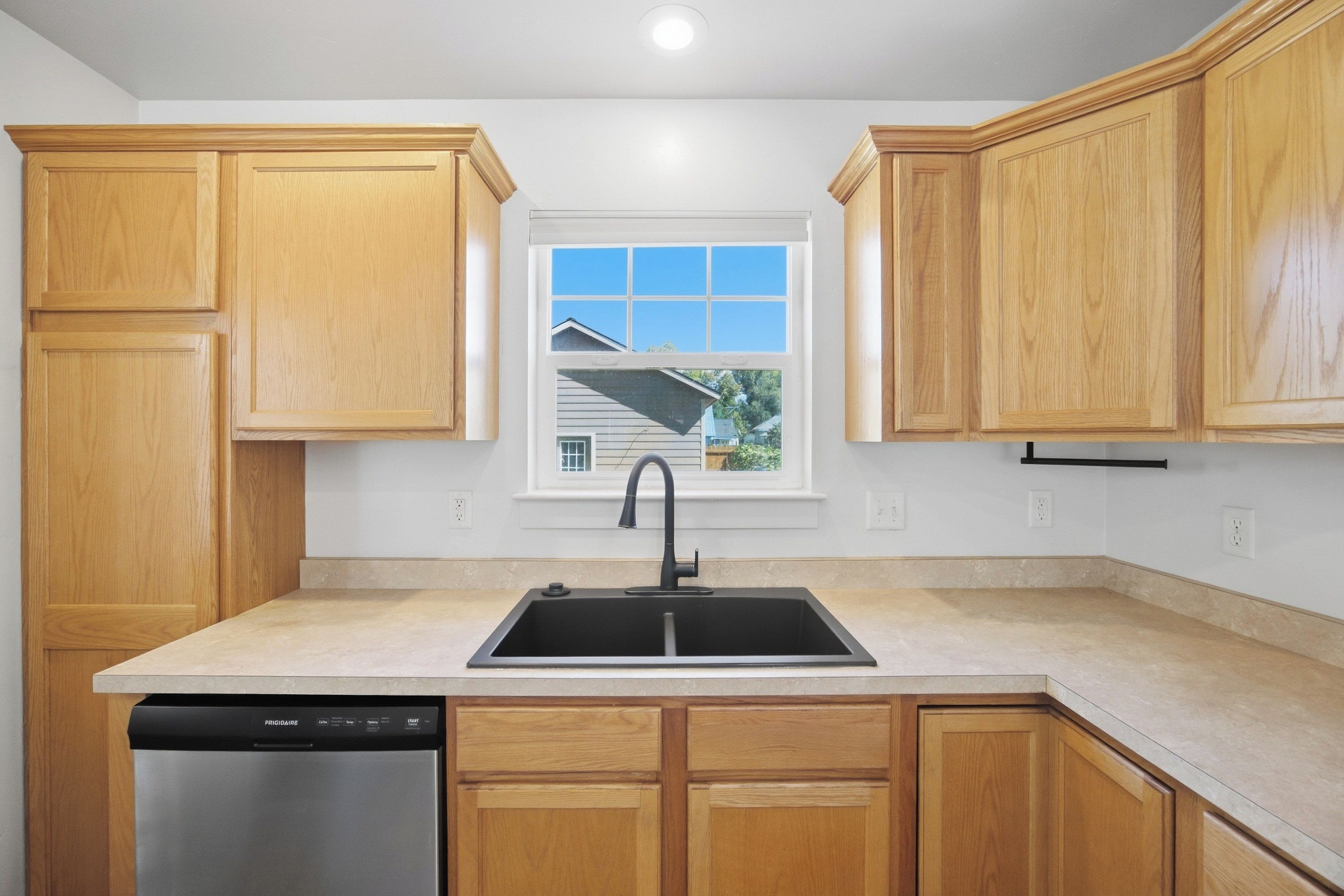 A kitchen with wooden cabinets, a black sink, and a dishwasher.