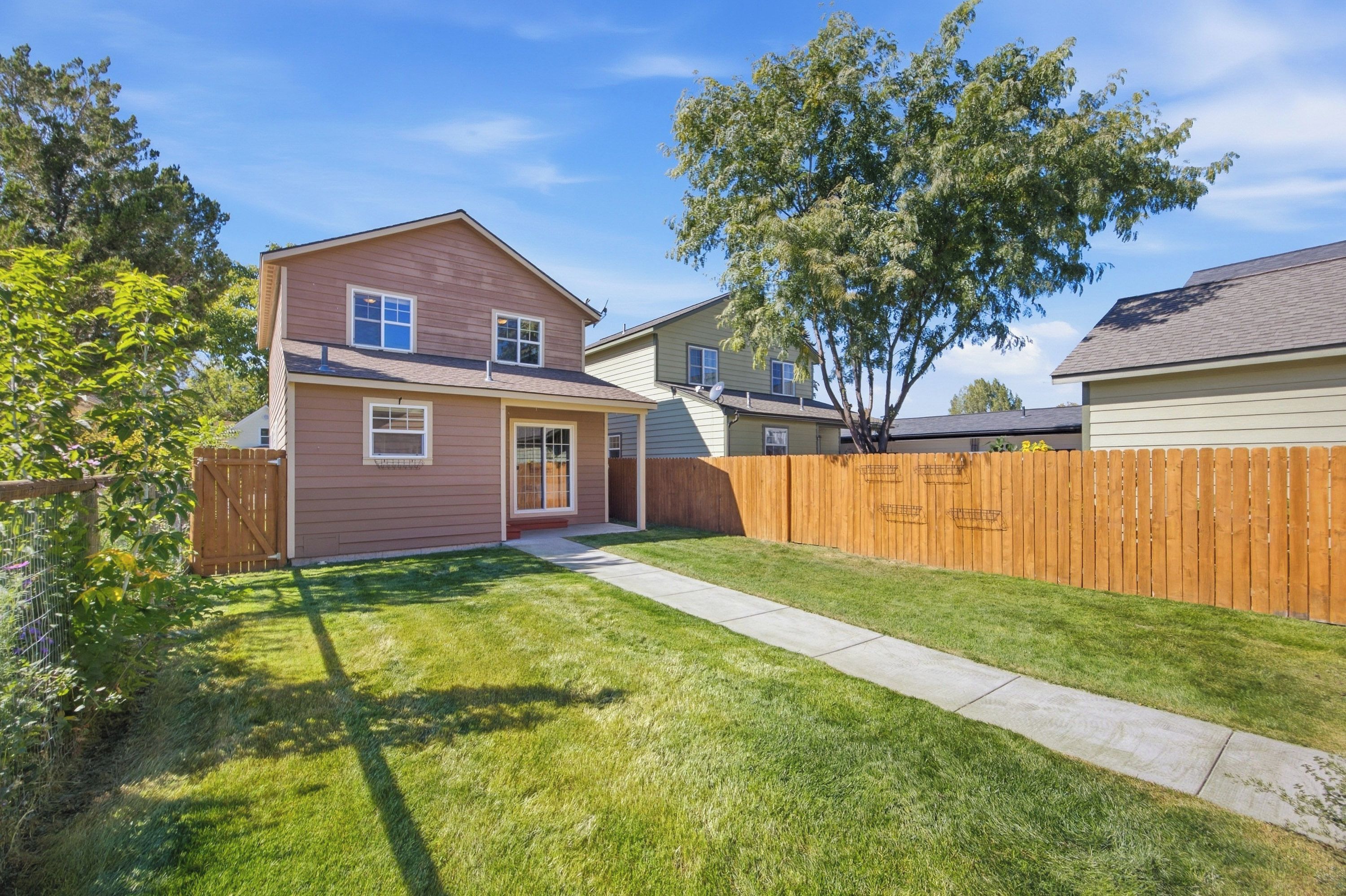 A two-story residential house with a front yard, a wooden fence, and a clear sky.