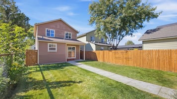 A two-story residential house with a front yard, a wooden fence, and a clear sky.