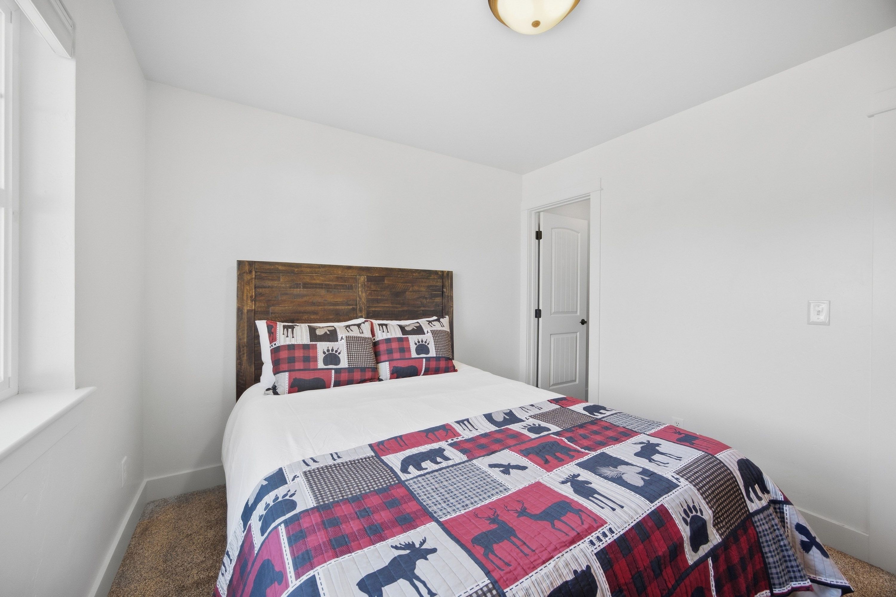 Un dormitorio con cabecera de madera, cama con colcha estampada de animales, ventana y puerta.