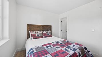 Un dormitorio con cabecera de madera, cama con colcha estampada de animales, ventana y puerta.