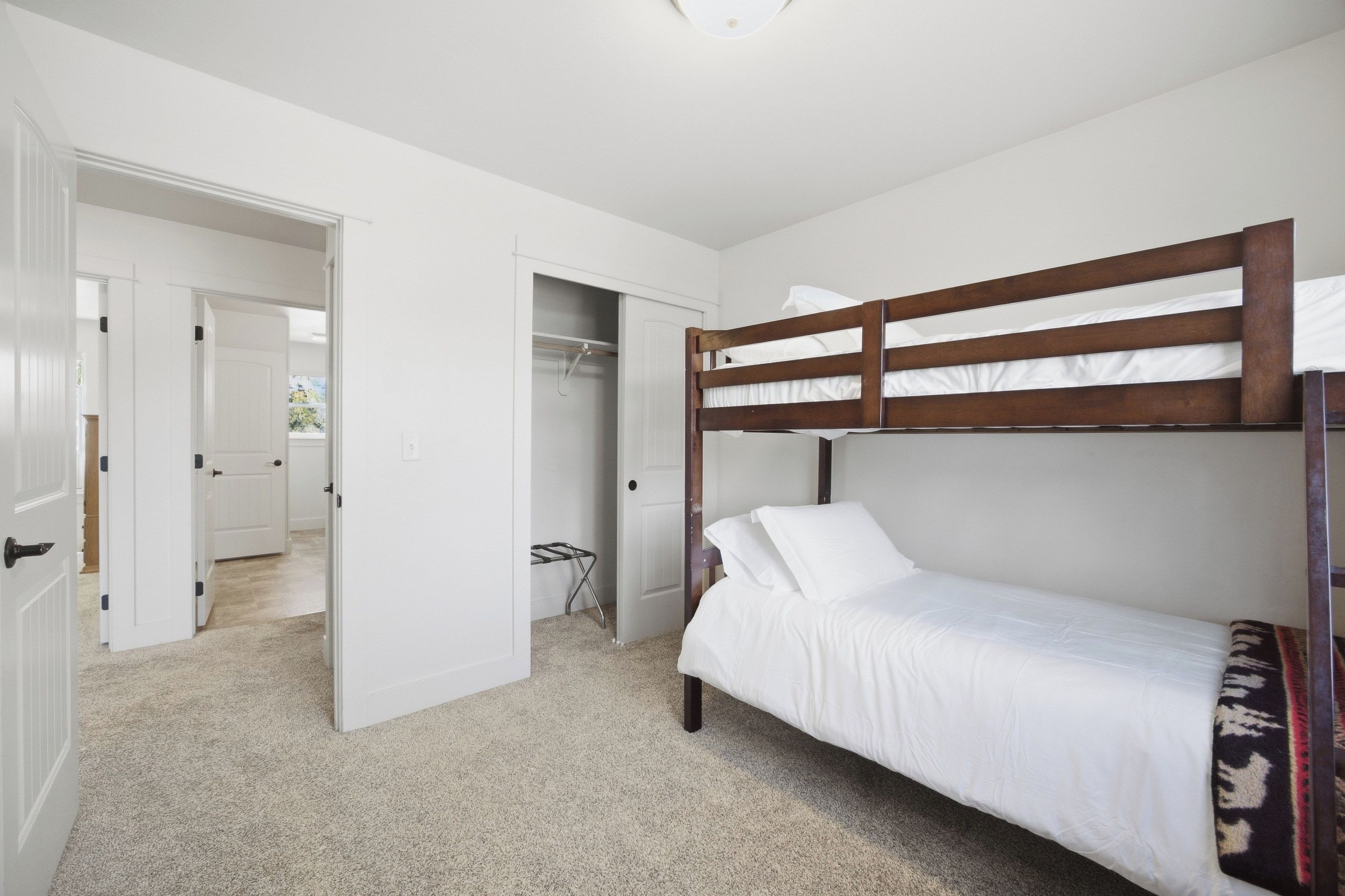 A room with a bunk bed, a door leading to another room, and a hallway.