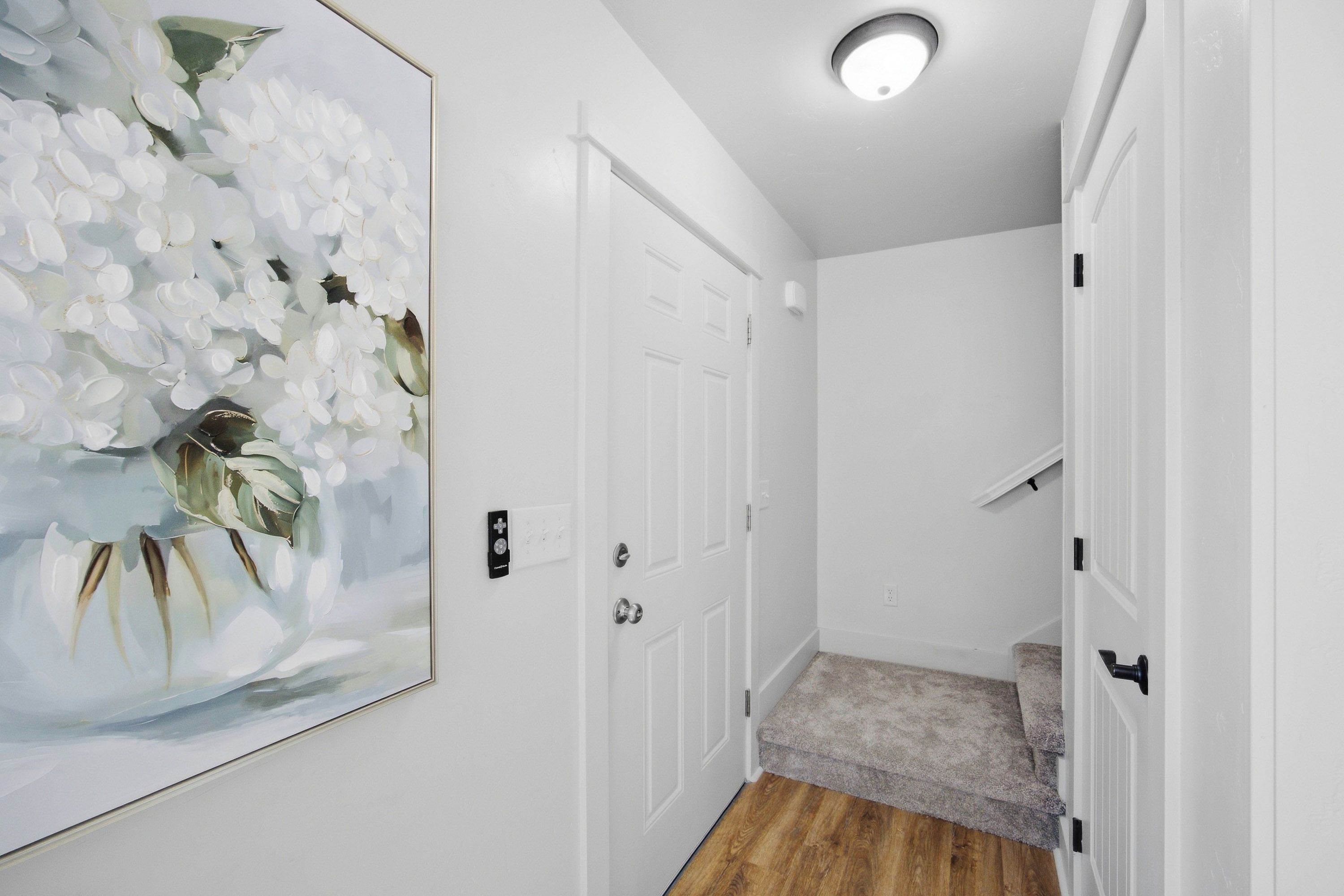 A hallway with white doors, a framed floral artwork, and a carpeted staircase.