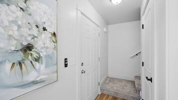 A hallway with white doors, a framed floral artwork, and a carpeted staircase.