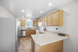 A kitchen with wooden cabinets, a stainless steel refrigerator, a dishwasher, a stove, and a countertop with a clock.