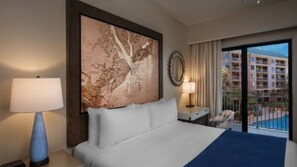 Un cuarto de hotel con una cama grande, un cuadro con un mapa en la pared, vista de un edificio a través de la ventana y una lámpara en la mesita de noche.