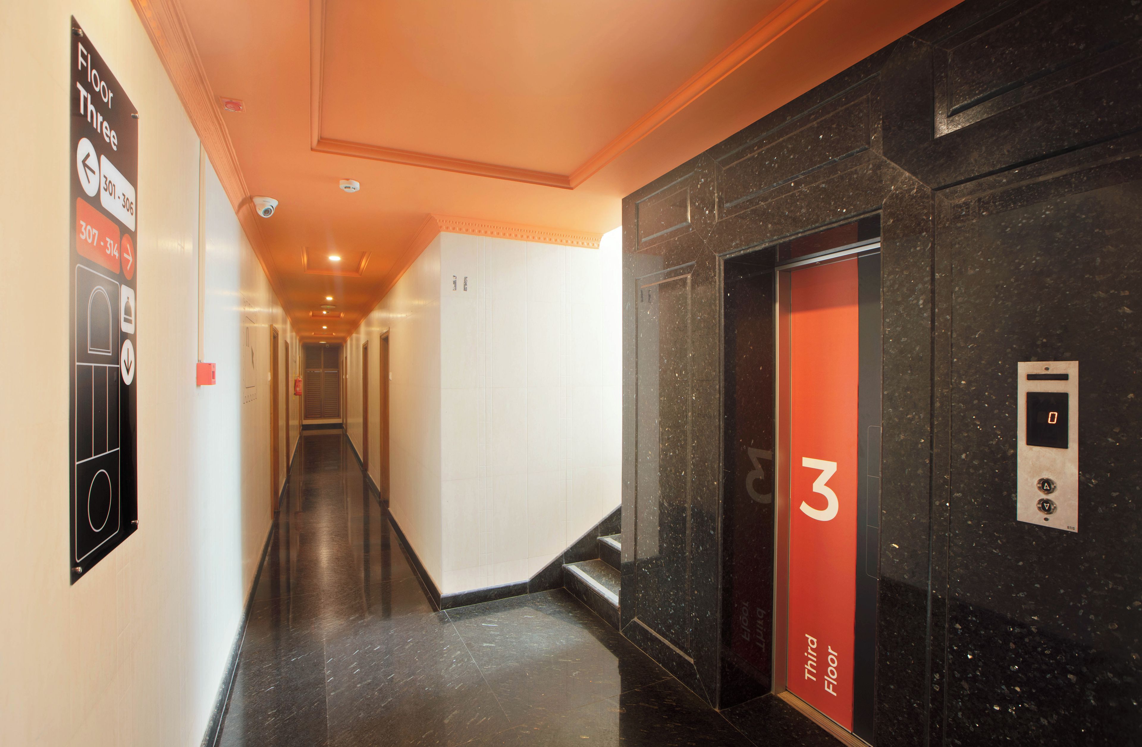 A hotel corridor with a third-floor elevator, a security camera, and a fire alarm.