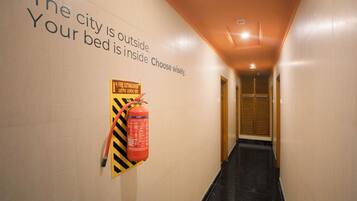 Un pasillo con un extintor instalado en la pared y un cartel con indicaciones de seguridad.