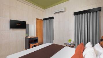 A hotel room with a bed, a television, a desk, a chair, a small table with a plant, and curtains.