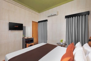 A hotel room with a bed, a television, a desk, a chair, a small table with a plant, and curtains.