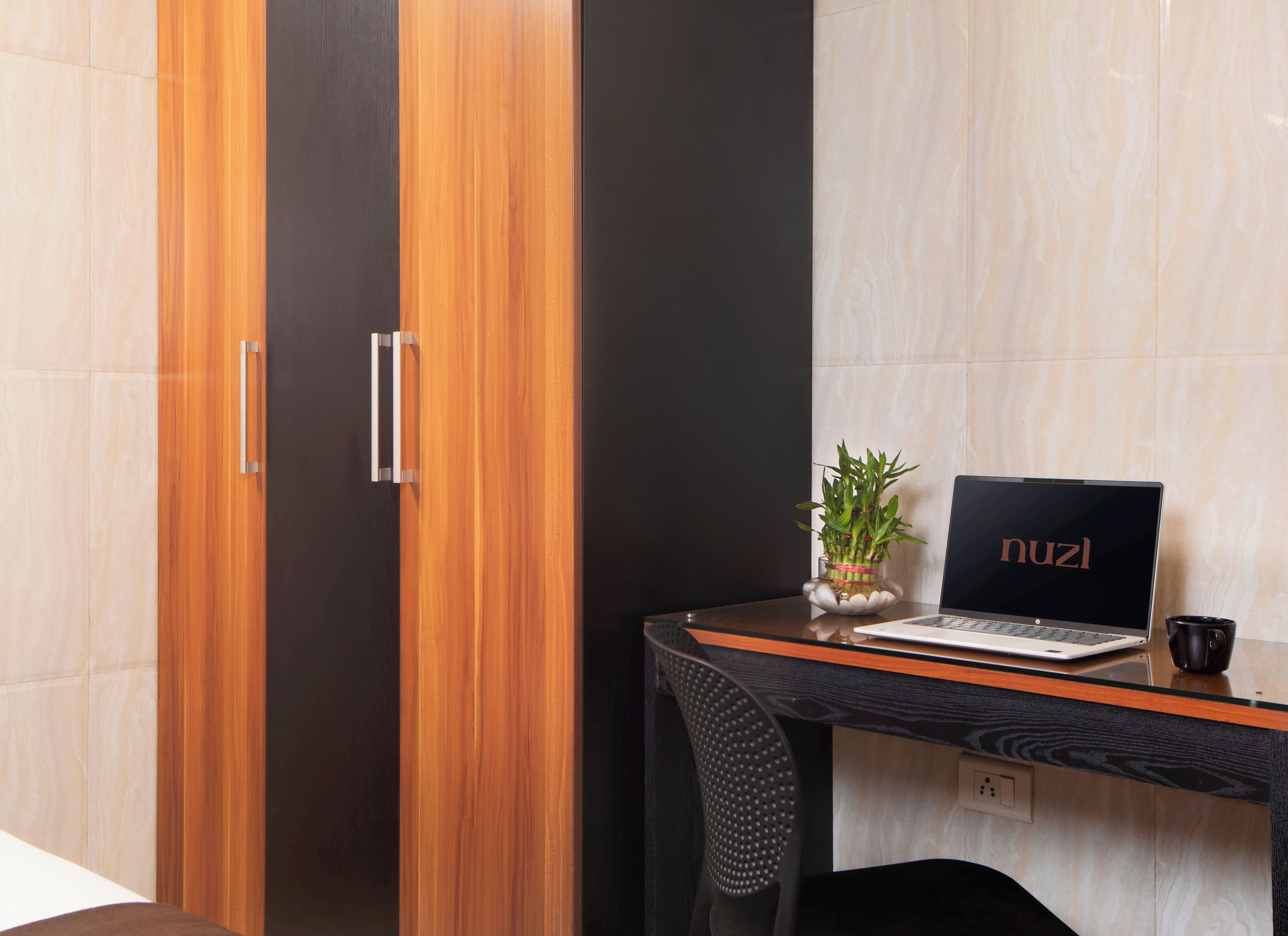 A modern room with a wooden wardrobe, a glass table with a laptop, a potted plant, and a black mug.