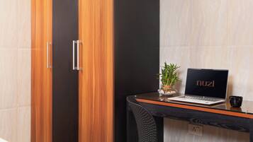 A modern room with a wooden wardrobe, a glass table with a laptop, a potted plant, and a black mug.
