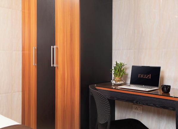 A modern room with a wooden wardrobe, a glass table with a laptop, a potted plant, and a black mug.