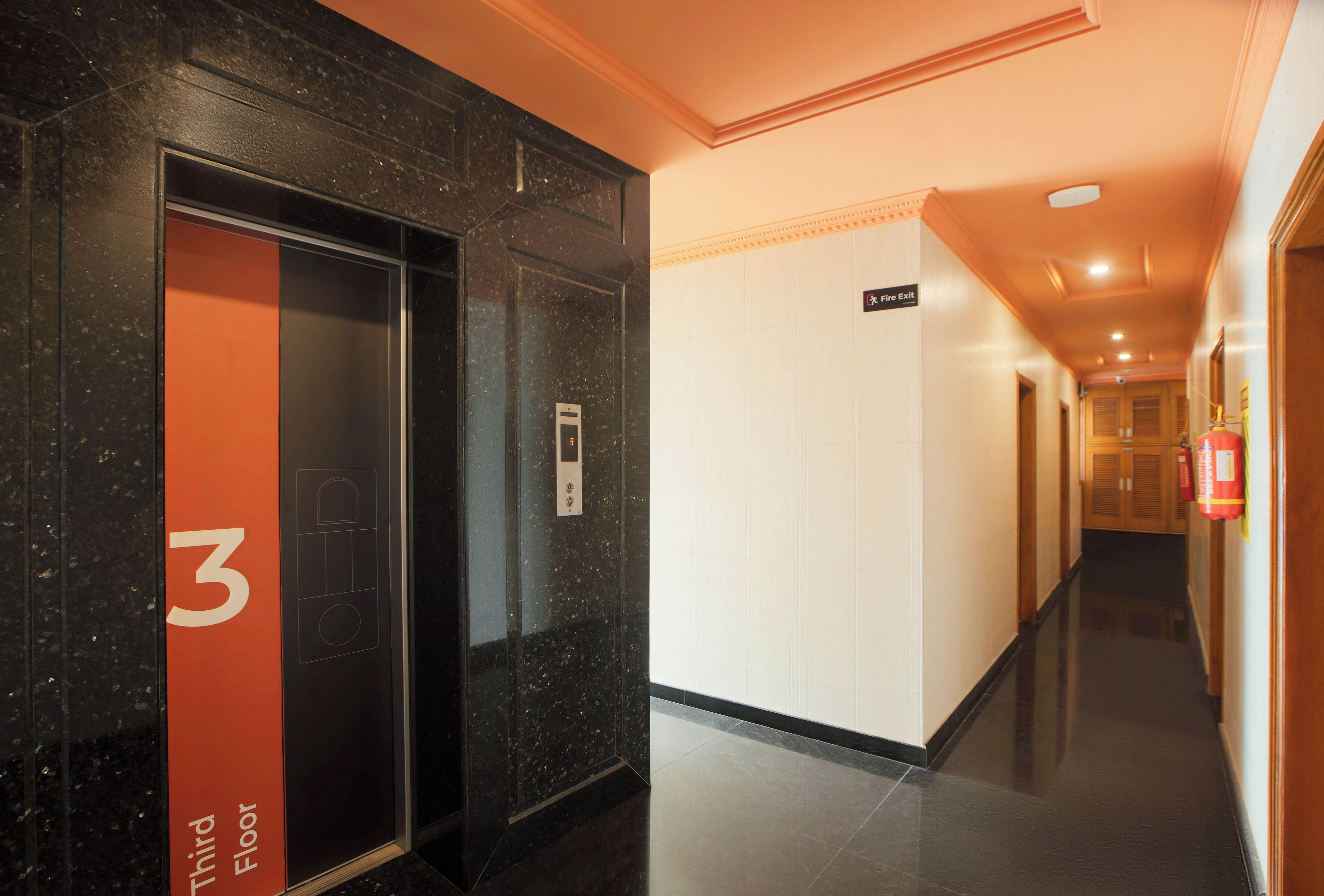 An interior corridor with a black elevator marked '3' and a fire exit sign.