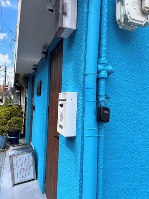 Eine blaue Außenwand mit einer weißen Anschlussdose und einem schwarzen Sicherheitselement.