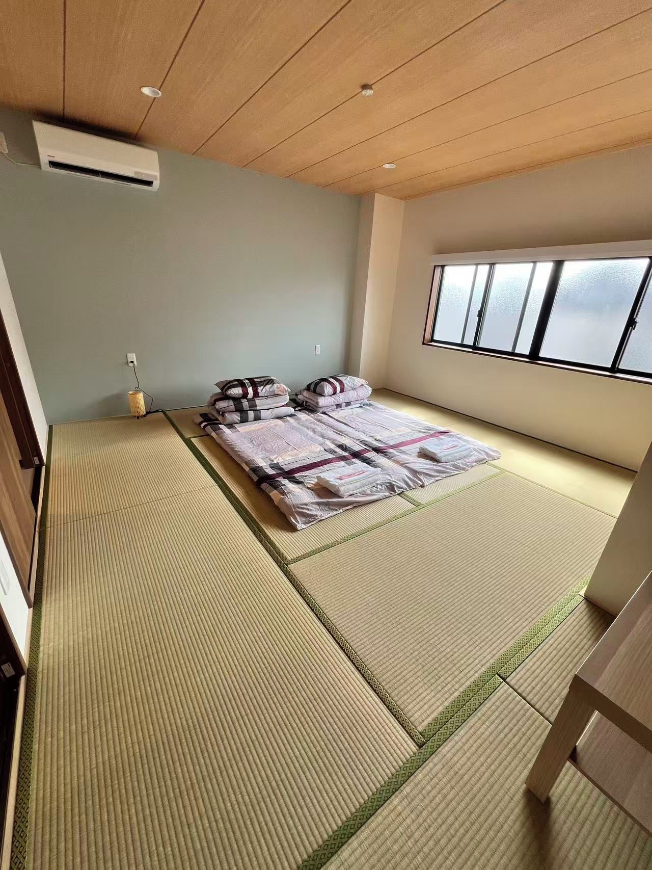 Una habitación con suelo de tatami, una cama con almohadas, una ventana y un ventilador de techo.
