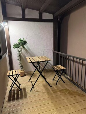 Ein Balkon mit einem Holztisch, zwei Stühlen, einem Blumentopf und einem Metallgeländer.