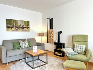 A living room with a sofa, a green armchair, a coffee table, a fireplace, and a painting of deer. - A cozy getaway at the Hirschzauber vacation rental with mountain views in the heart of Oberstdorf (Oberstdorf)