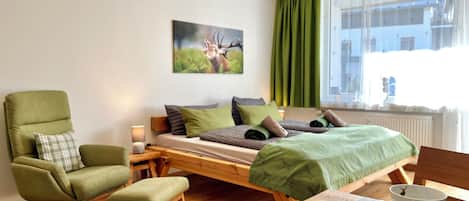 A room with a bed, a chair, a table with a cup and saucer, and a painting on the wall.