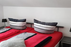 A bed with red bedding and striped pillows, a bedside table with a lamp, and a plain wall. - 2-room apartment with a fantastic view (Winterberg)
