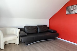 A living room with a curved sofa, a chair, and a red accent wall. - 2-room apartment with a fantastic view (Winterberg)
