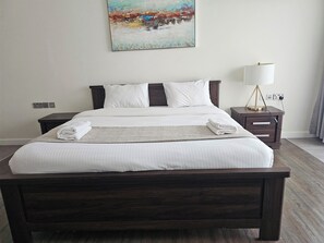A neatly made bed with white linens, a dark wooden headboard, and a small bedside table with a lamp. - Cozy 1-bedroom apartment in serene Nairobi with fitness room (Nairobi)