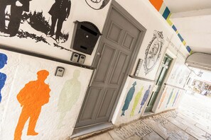 Ein Gang mit einer Tür, einem Briefkasten und einer Wand mit Schattenbildern von Personen.