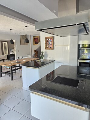 A modern kitchen with a central island, a dining area with a wooden table, and a living space with a sofa and TV.