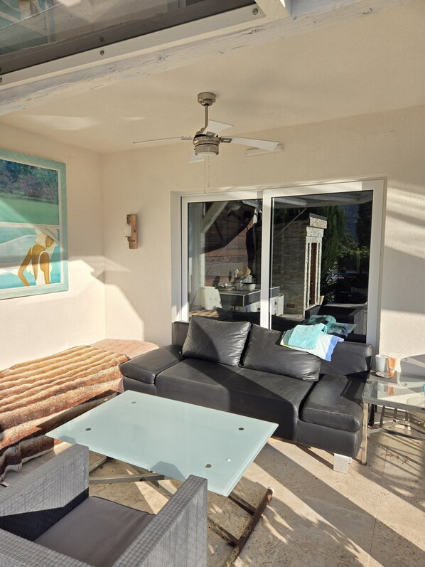 An outdoor seating area with a black sofa, a glass table, and a ceiling fan. - Villa with a hot tub, fireplace, and views of the Vosges (Walbach)