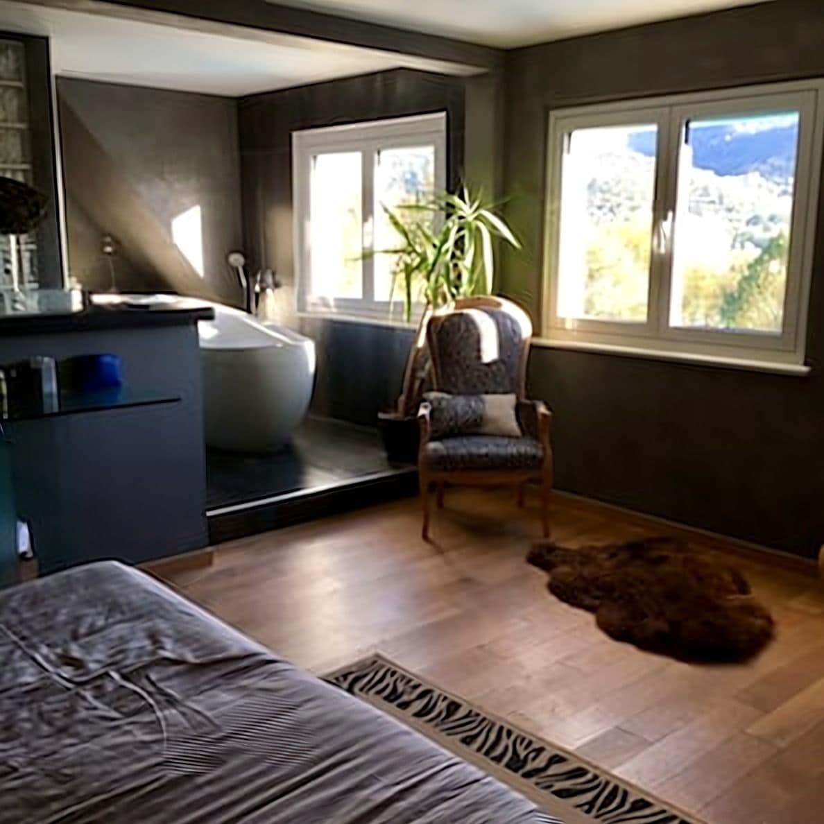 Une salle de bain moderne avec une baignoire, un lavabo et une chaise. Il y a une fenêtre donnant sur l’extérieur.