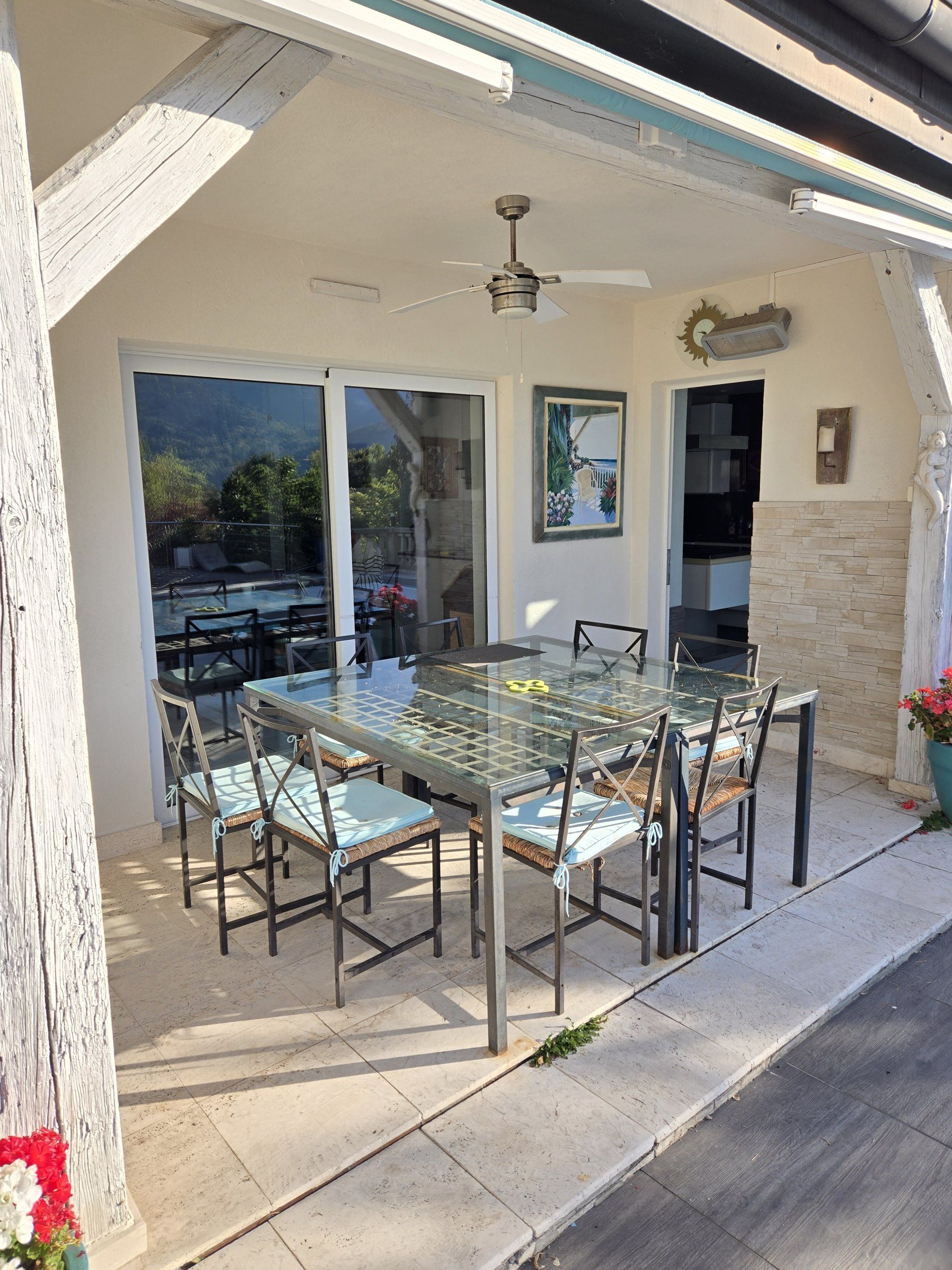 Une terrasse extérieure avec une table et des chaises à plateau en verre, un ventilateur de plafond et une vue sur l’extérieur.