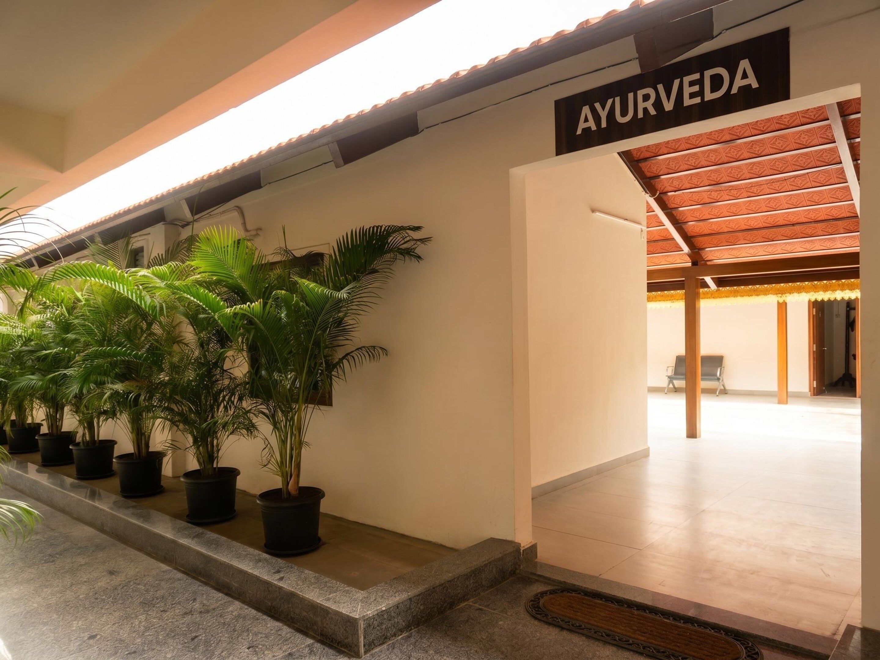 A hallway with potted plants, a sign reading 'AYURVEDA', and a covered area with chairs.