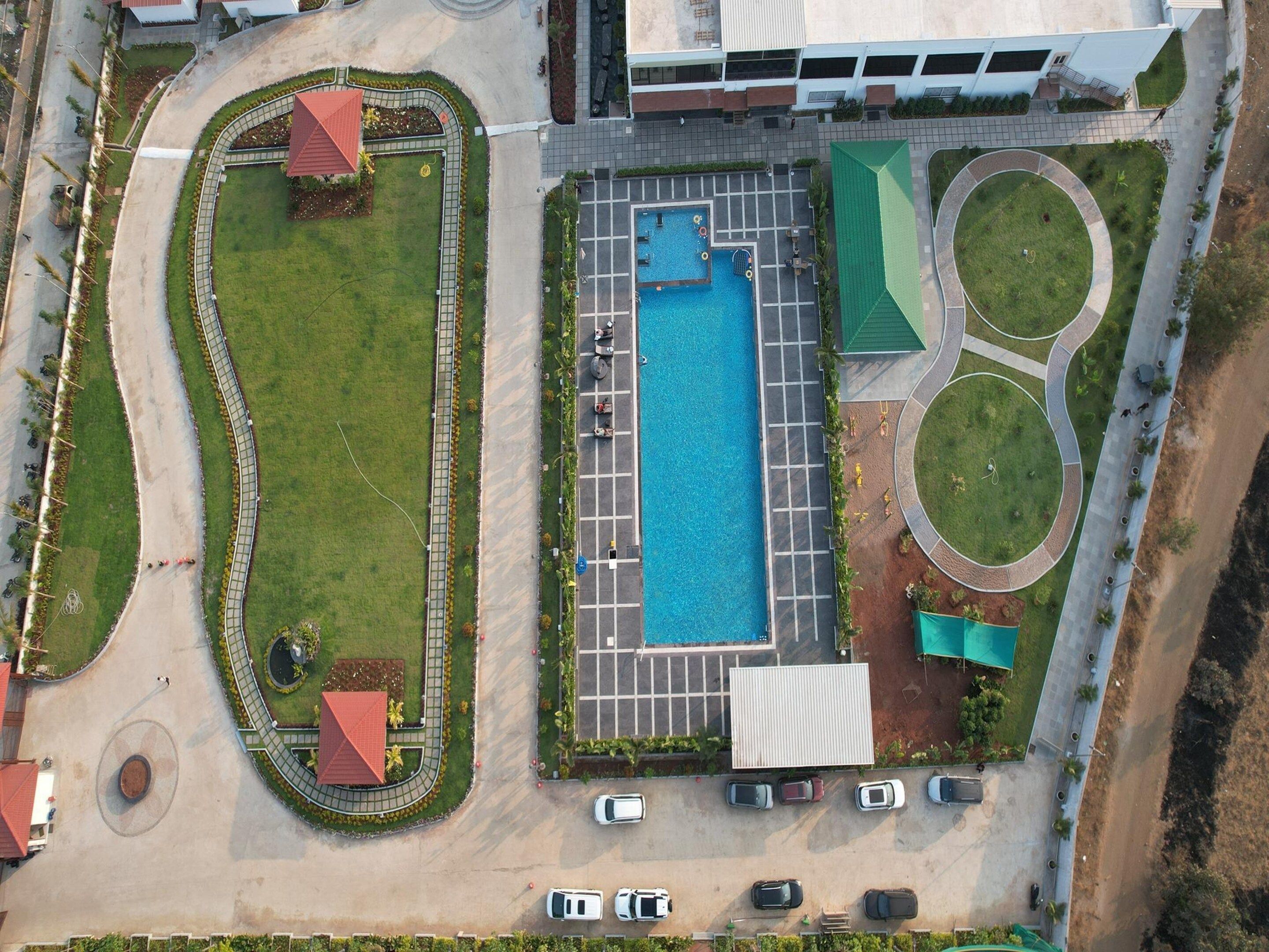 An aerial view of a property with a swimming pool, parking area, and landscaped gardens.