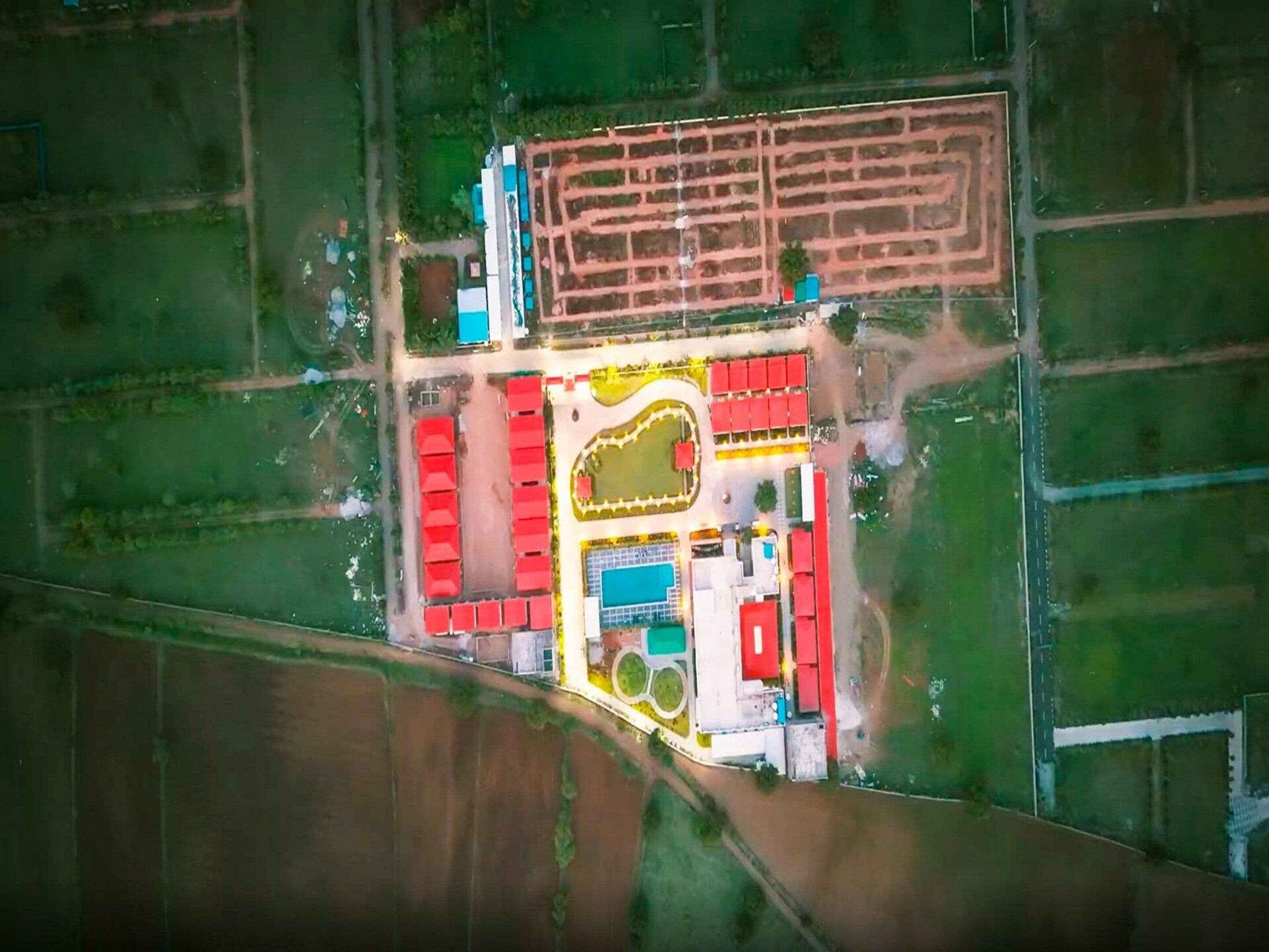 An aerial view of a property with distinct rectangular and square buildings, a central open area, and surrounding green fields.