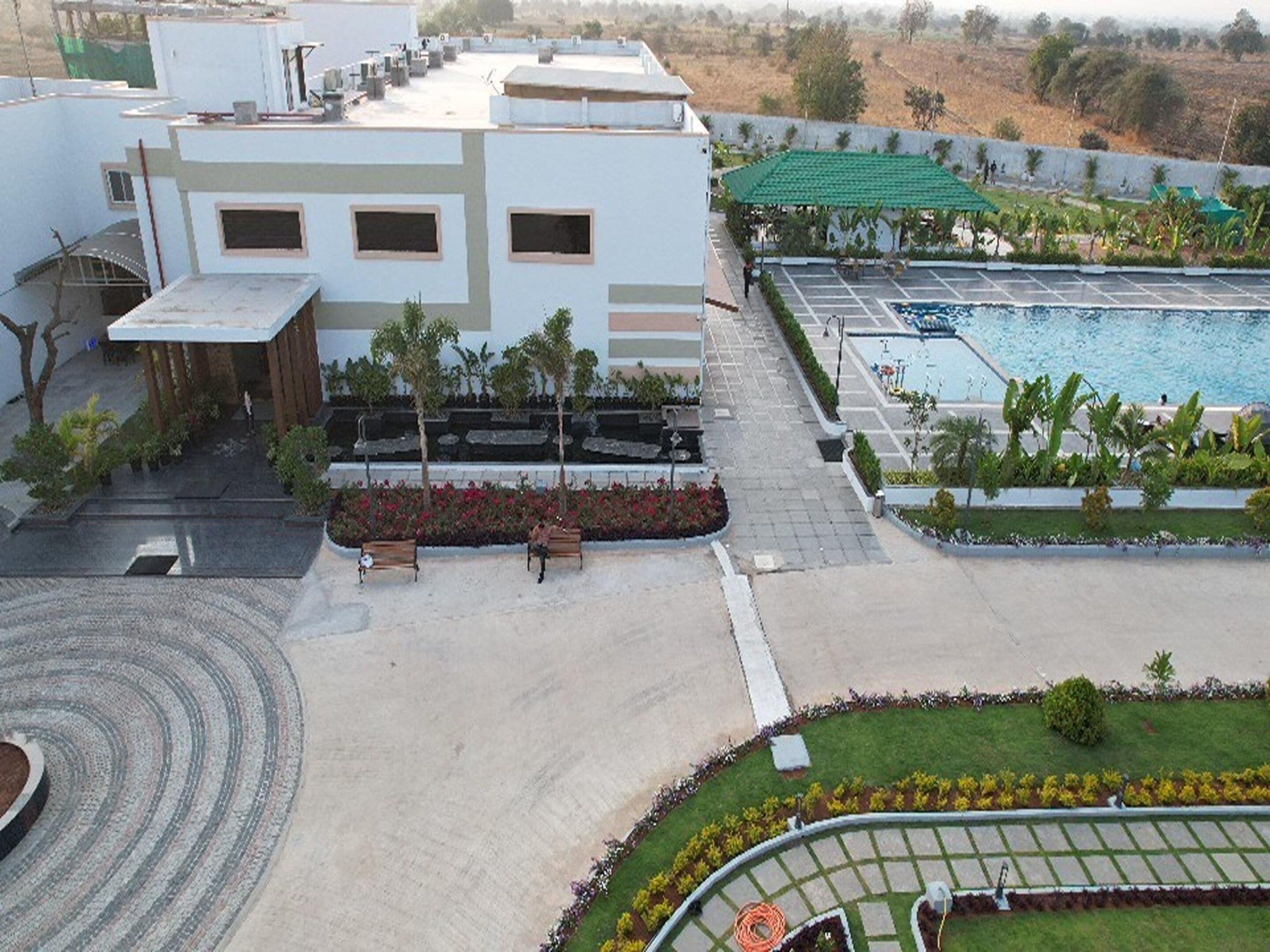 Hotel com piscina no terraço, jardim ajardinado e área de estacionamento.