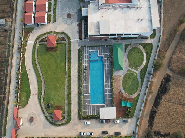 An aerial view of a property with a swimming pool, parking area, and landscaped gardens.