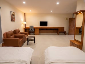 Habitación de hotel con sofá, una mesita, televisión, banco de madera y espejo.