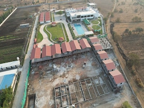 An aerial view of a building complex with multiple structures, including a swimming pool, landscaped areas, and a large open construction site.