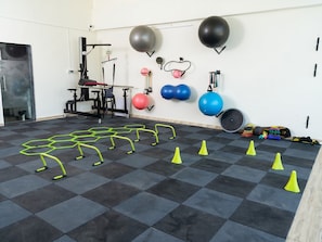 A gym with exercise equipment, including a squat rack, medicine balls, and resistance bands.