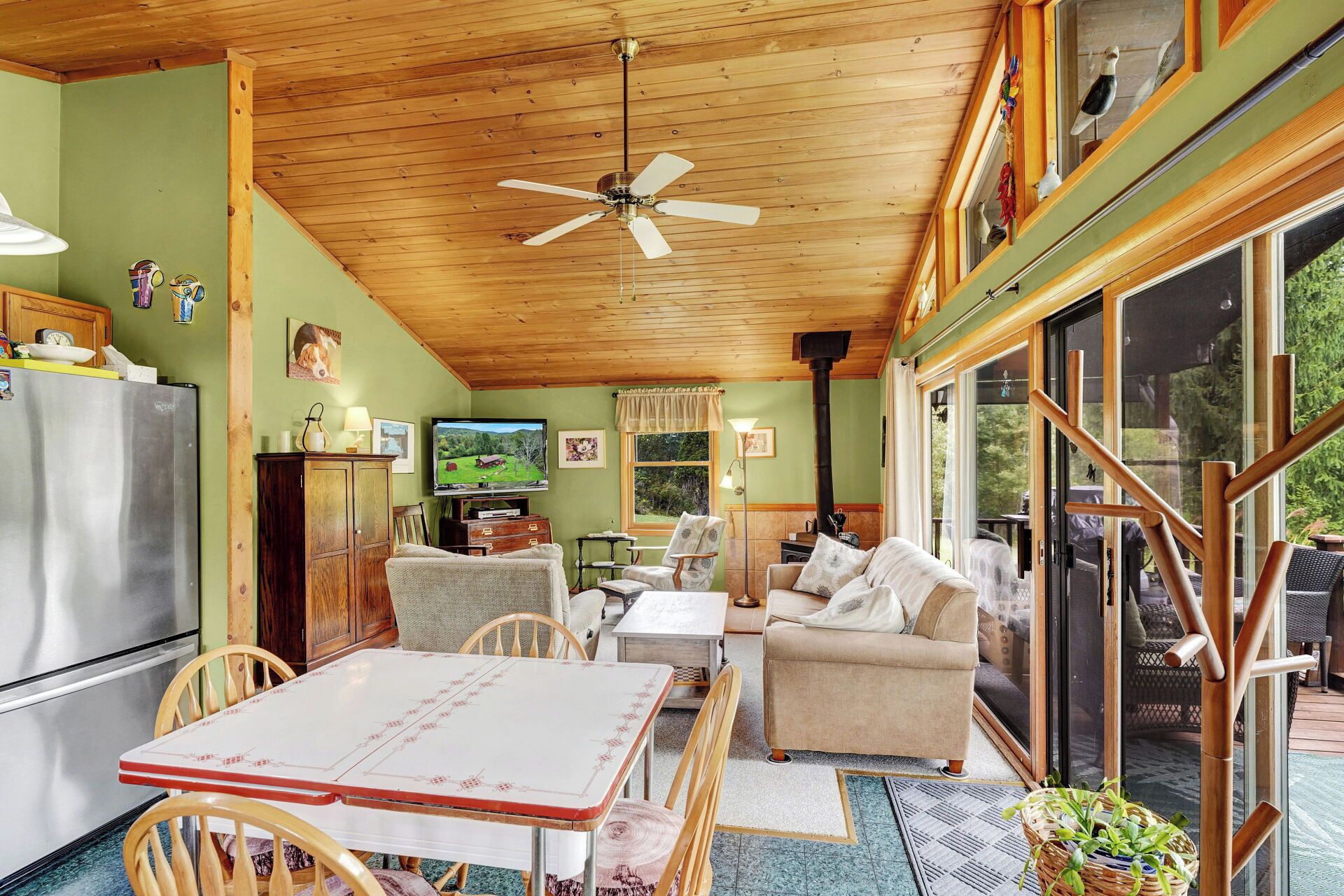 A cozy living room with a wooden ceiling, a television, a sofa, a table, and a refrigerator.