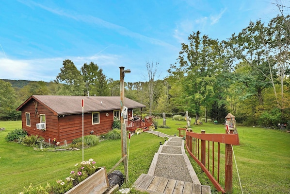 A wooden cabin with a porch, surrounded by a well-maintained lawn and trees.