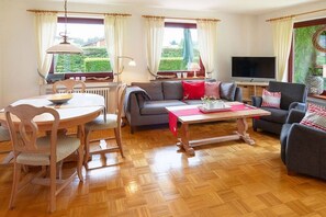 Ein Wohnzimmer mit einer Couch, Sesseln, einem Esstisch und einem Fernseher.