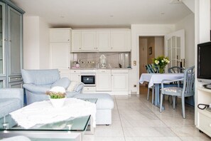 A modern living room with a sofa, a glass coffee table, and a dining area with a table and chairs. - Beach Villa Atlantic App. 03 (Norderney)